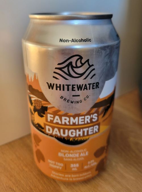 A can of Whitewater Brewing Co. Farmer's Daughter Non-Alcoholic Blonde Ale, with a silver top and a label featuring a mountain and river scene, a turtle, and orange and brown colors.