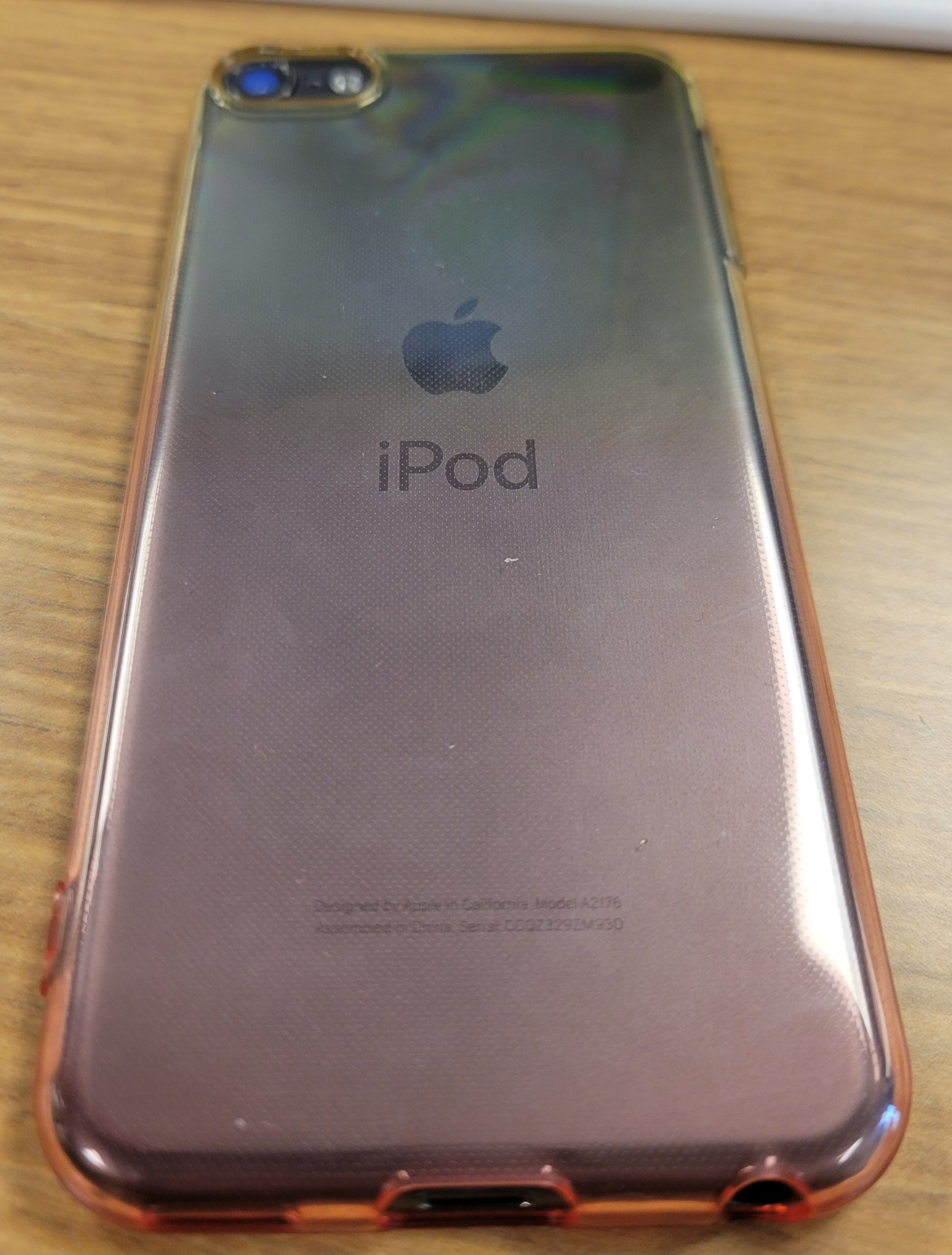 The back of a 7th-generation iPod Touch. The space grey backing is inside an orange-yellow gradient clear case.
