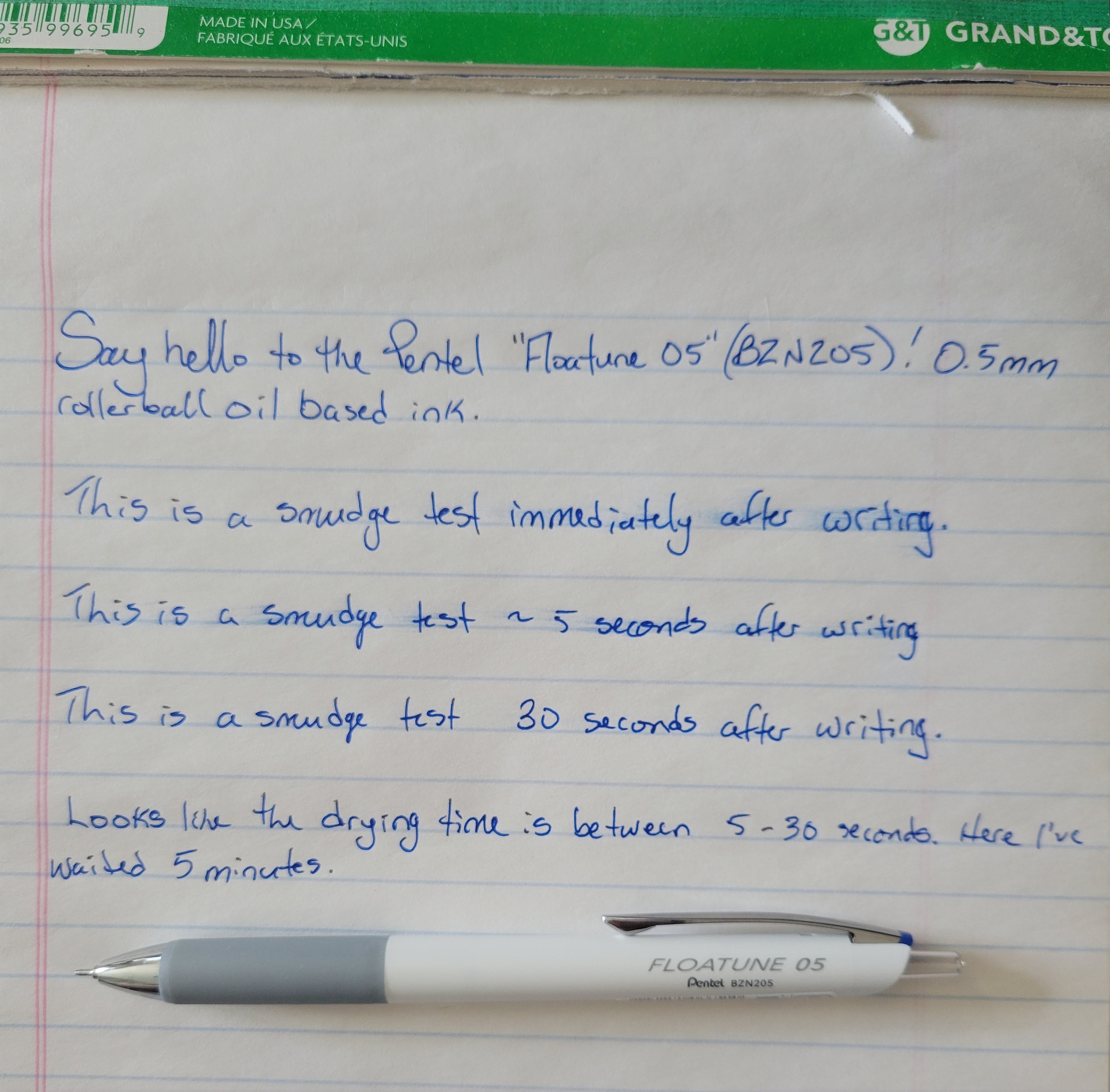 Several lines of text testing out the ink of a Pentel Floatune 05. The pen itself is placed below the ruled lines.