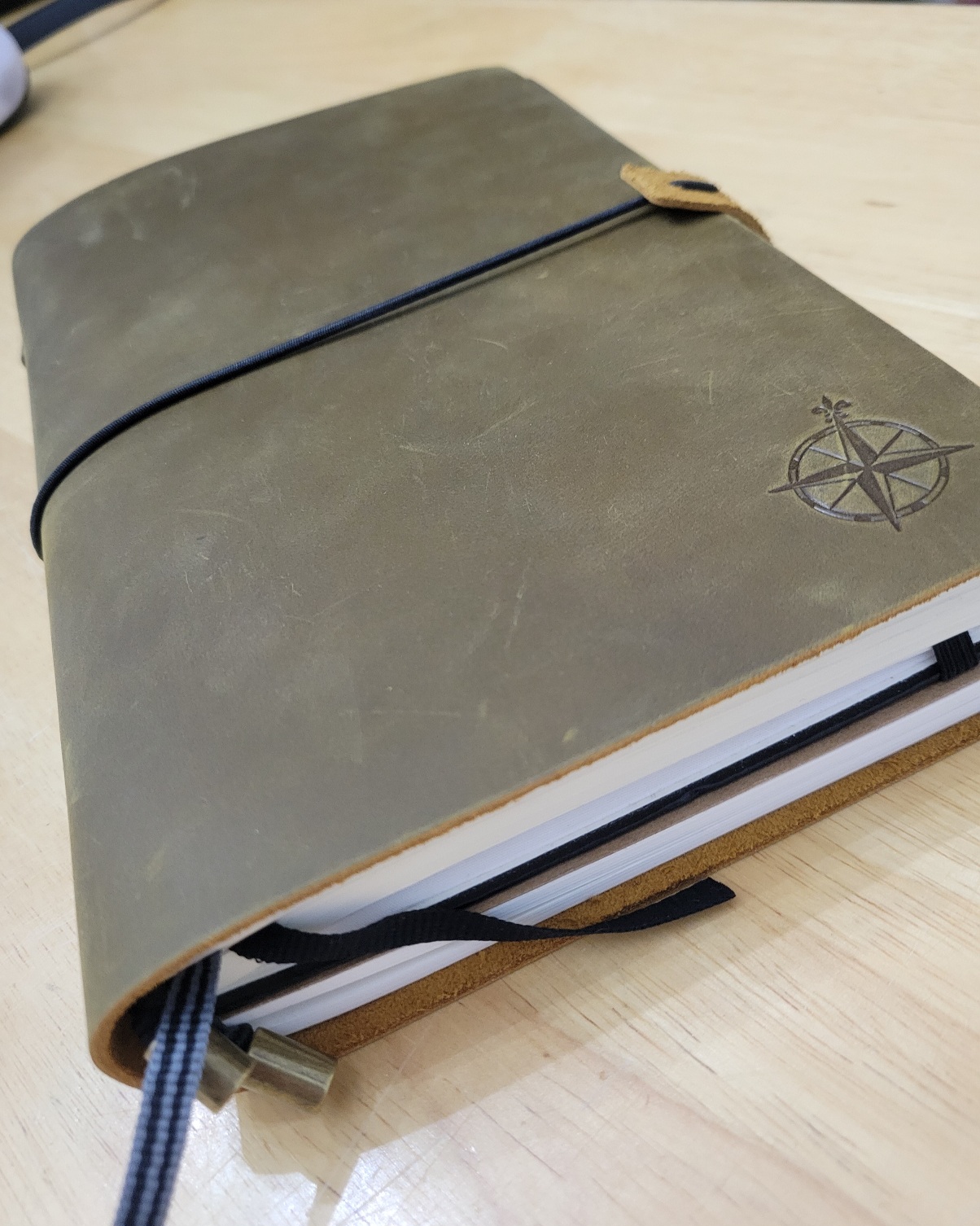A leather notebook cover containing a thick hardcover notebook and thin softcover notebook; there is a compass in the lower right corner of the notebook and some ribbon bookmarks in the centre of one of the notebooks.